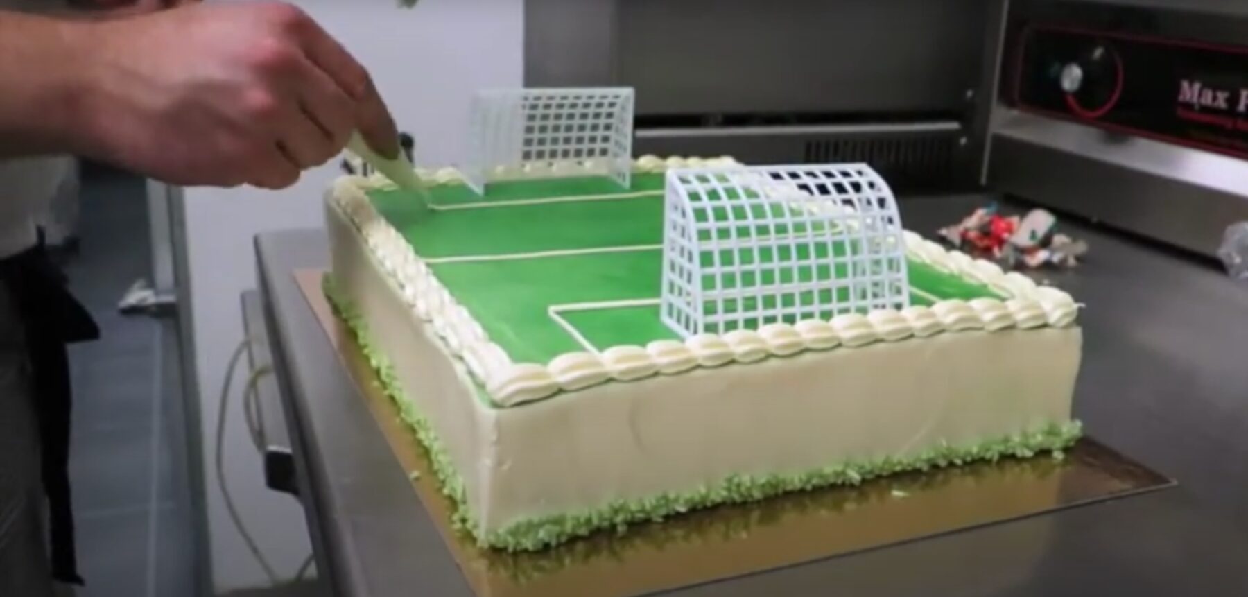 Een banketbakker spuit de laatste details op een voetbaltaart in de bakkerij